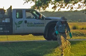 A worker wearing gloves and a hat is applying a lawn treatment near a Bob Jenkins (Now Barefoot) Pest & Lawn Services truck.